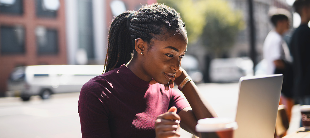 Woman with braids using a laptop at an outdoor cafe